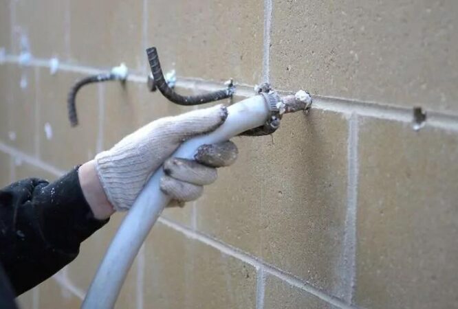 A person using a hose to inject insulation material into the cavities of a brick wall, demonstrating a technique used by Insul-Techs Inc in Martinez for improving energy efficiency.
